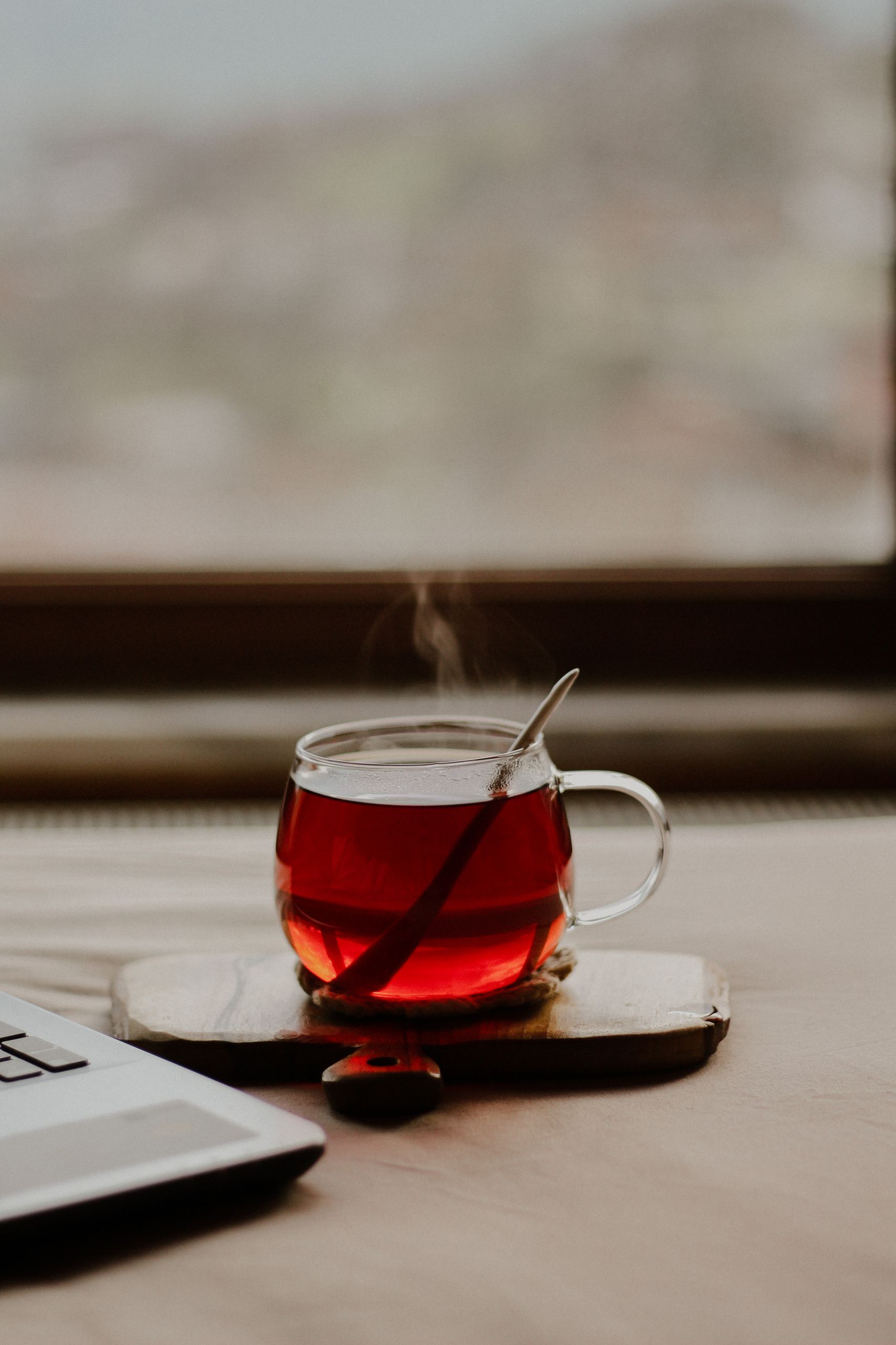 A steaming glass cup of tea sitting on a saucer in a cozy indoor setting.